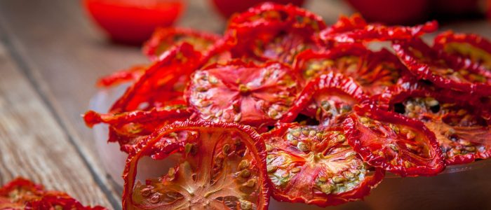 Side view close-up dried tomatoes in plate and fresh tomatoes on wooden table